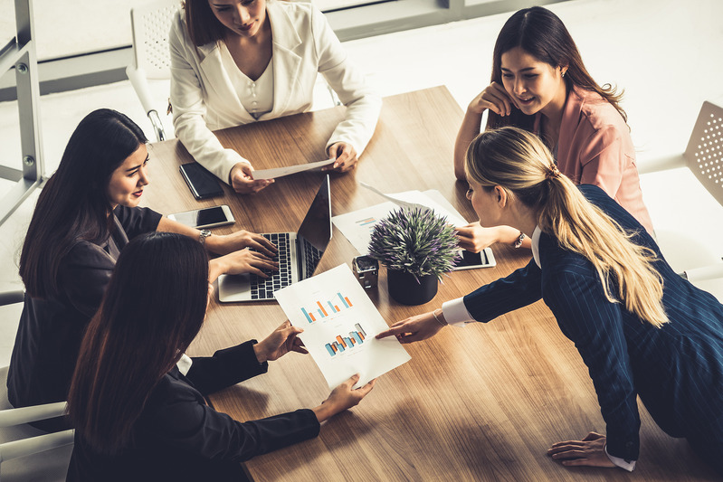 Businesswoman in group meeting discussion with other businesswomen colleagues in modern workplace office with laptop computer and documents on table. People corporate business working team concept.